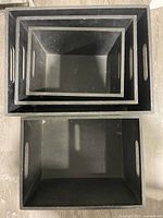 Top-down view showing the four nested rectangular black wooden boxes with built-in handles.