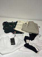 Clothing folded and laid flat showing variety of tops, shorts, and dress. Tags visible showing new condition.