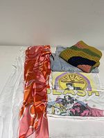 Silky orange-pink patterned fabric piece alongside folded light-wash jean and crochet top/skirt, white graphic tees are visible underneath.