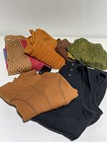 Four folded knitted and fabric tops and skirts in autumn colors with one black utility dress, all displayed on white surface.