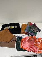 Overview of folded clothing including patchwork fabric, brown toned tops, knit pants and silky patterned top