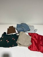 Photo of seven folded clothing items laid out on a white surface, including various dresses, shorts, vests, and tops in different colors and fabrics.