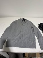 Light grey Calvin Klein pullover laid flat, shows front, long sleeves, ribbed collar and cuffs, quarter-zip.