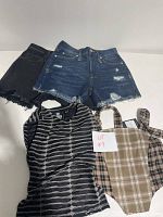 Two pairs of distressed denim shorts in dark washed and black, one striped top with collar and buttons, and a beige plaid sleeveless top arranged on a white surface with a lot number card.