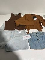 Photo displaying brown fitted tank top and matching cropped zip-up jacket along with light and classic blue denim shorts, tagged as size US 24.