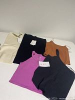 Tops and shorts laid out flat on a white background showing tag details and various colors such as black, magenta, cinnamon, cream.