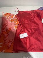 Close-up photo showing two satin dresses, one with a fiery orange and pink print and the other solid red, labeled as Lot 17.