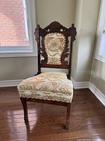 Front angled view of the antique wood needlepoint chair showing carved wood frame and floral upholstery on backrest and seat.