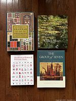 Four hardcover art books arranged on wood floor: The Grammar of Ornament, Claude Monet, Handbook of Pottery & Porcelain Marks, The Group of Seven