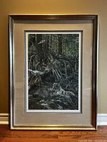 Framed print artwork seen from the front showing the full image of the lynx resting in a forest environment with tree roots and bluejays