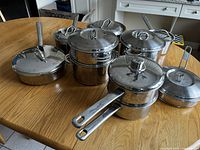 Front and top view of set of 8 assorted metal pots and pans on wooden table.
