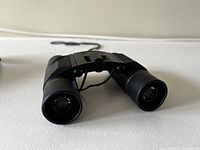 Close front view of black compact Bausch & Lomb Legacy 10x25 binoculars with central focus wheel and textured grips.