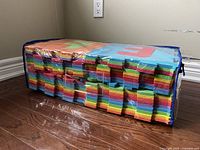 Side view of packaged colorful foam interlocking mats stacked horizontally inside a clear plastic bag with a blue zipper.