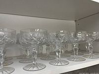Shelf display of 24 clear antique crystal champagne coupes, showing detailed cut crystal patterns on bowls and stems