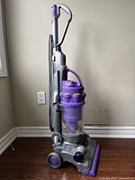 Side view of the upright vacuum showing handle, cord wrapped on side, dust bin and wheels