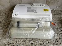 Closed view of Foodsaver vacuum sealer machine with vacuum seal rolls wrapped in plastic on front.