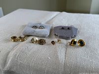 Six pairs of gold-tone earrings arranged on fabric surface