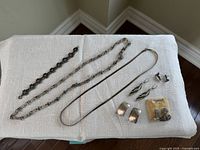 Eight pieces of assorted silver jewelry arranged on a white cloth: 1 bracelet, 2 necklaces, 4 pairs of earrings, 1 brooch.
