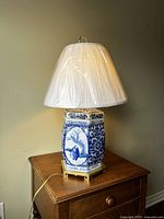 Front view of the porcelain blue and white lamp with white pleated shade on wooden surface.