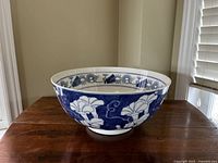 Side view of large blue and white porcelain bowl showing floral and vine pattern on exterior displayed on wooden surface near window.