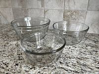 Two sets of three nested clear glass mixing bowls shown on countertop.