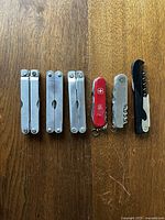 Set of six pocket multitools arranged on wooden floor, showing closed tools from the front