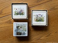 Two sets of floral print coasters with cork back and one set of golf print coasters on tile shown on a wooden surface.