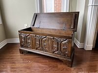 Chest with hinged lid open showing interior storage space and carved front panels