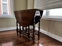 Wooden drop leaf table folded with single drawer and turned legs visible.