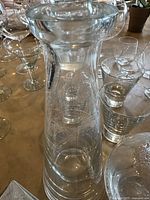 Photo showing the tall cylindrical etched glass decanter with stopper; other glasses visible in the background