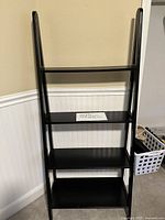 Front view of black four shelf arched bookcase against beige wall and white wainscoting.
