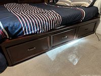 Full view of bed frame with navy blue striped bedding showing three under-bed storage drawers on one side.