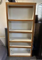 Photo of white shelving unit with oak wood finish and four shelves, showing the overall structure and condition.