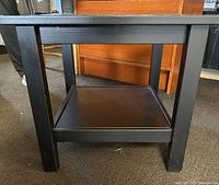 Side view of the black square side table showing lower shelf and four legs.