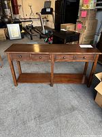 Full view of the wood console table showing four drawers and bottom shelf, placed in a room with other furniture and moving boxes