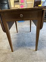 Front view of wood table with one drawer and tapered legs, showing drawer pull and table legs.