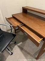 Wooden desk with two shallow drawers open and showing interior, top surface with minor marks, raised shelf on top