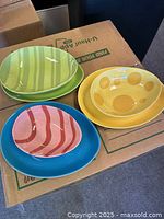 Photo of 6 colorful egg-shaped dishes resting on a box, showing green, yellow, blue, and pink dishes with various patterns.