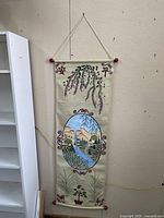 Full view of fabric wall hanging showing Asian inspired art with purple flowers, scenic landscape, bamboo, and potted plant