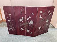 Four-panel Asian lacquer wood plaque with silver inlay designs of birds and flowers spread out on floor for full view.