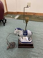 Full view of the blue and white porcelain horse lamp with visible cord, socket, and mounted on wooden base.