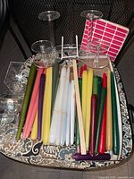 Top view photo of taper candles in various colors and designs alongside clear plastic candle holders and cardboard boxes with labels.