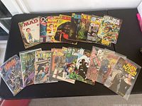 Top-down view of assorted comics spread out on a table, showing vintage MAD Magazine, 2000 AD, Eerie, Airboy, Alien Nation and other comics in varied conditions.