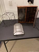 Three display items including wooden wall-mounted cabinet, glass display case, decorative metal stand on a black table