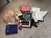 Overview of assorted fabric items including patterned valances, doilies, embroidered pieces, and a blue fabric box holder.