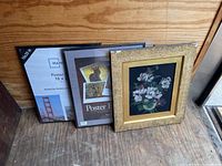 Photo showing a framed floral art print with a gold decorative frame and two new black wooden poster frames in packaging with 16x20 size indication.