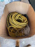 Box partially filled with thick yellow twisted rope and tan thin cords inside a cardboard box on the floor.