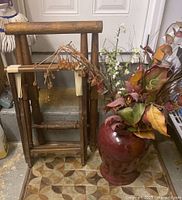 Photo showing two wooden folding butler trays and large maroon ceramic floor vase with assorted artificial plants inside.
