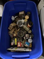 Top-down view of blue plastic tub filled with assorted hardware items including jars and boxes of nails, screws, and other fasteners.