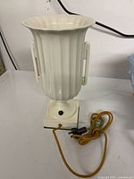 Full view of the white ceramic Lenox style table lamp showing the fluted vase-shaped body on a square base with attached brown cloth-covered power cord.